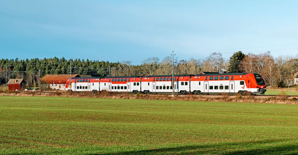 Er1 åker på rälsen en vårdag, en grön åker och blå himmel.