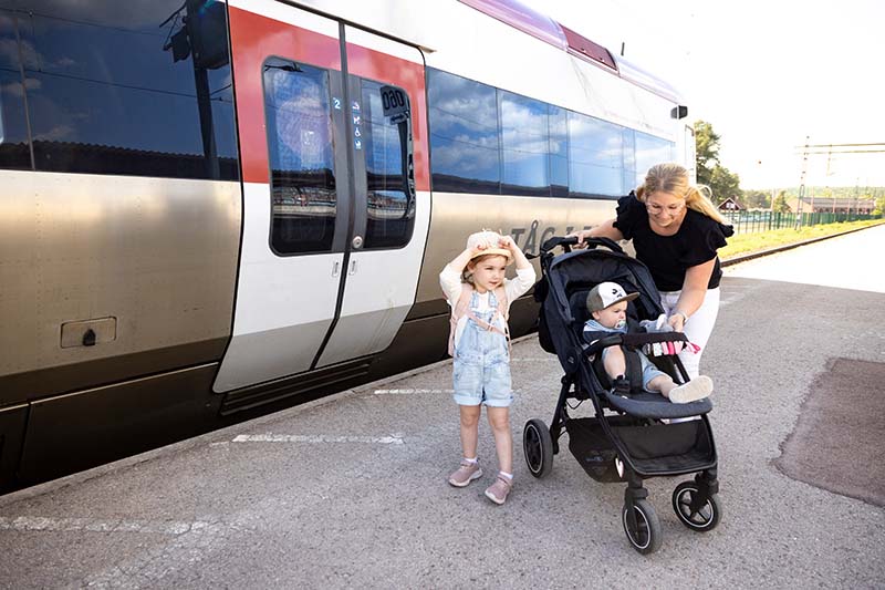 Mamma står på perrongen med sina två barn och barnvagn